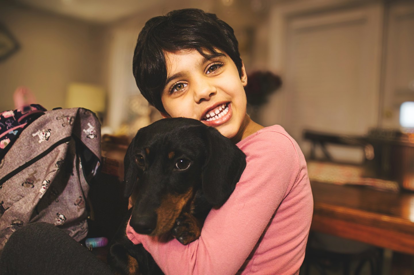 Child in pink shirt hugs a dachshund dog.