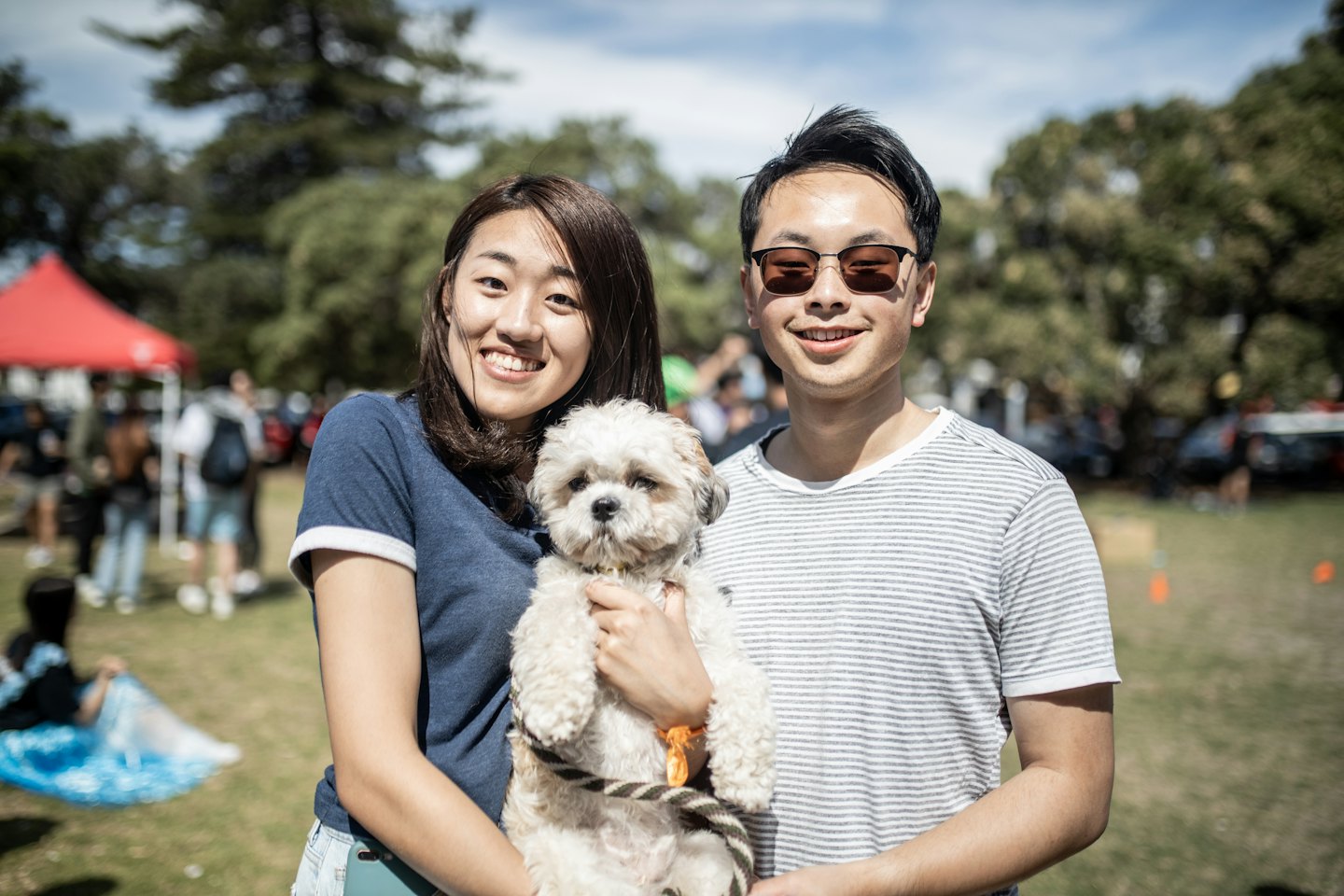 A smiling couple holding their small fluffy white dog outside.